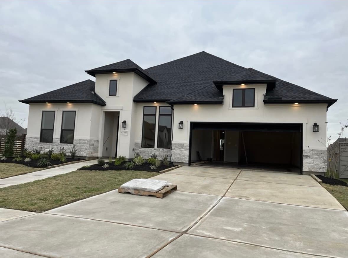 Modern white stucco house with black trim, stone accents, and an open garage.
