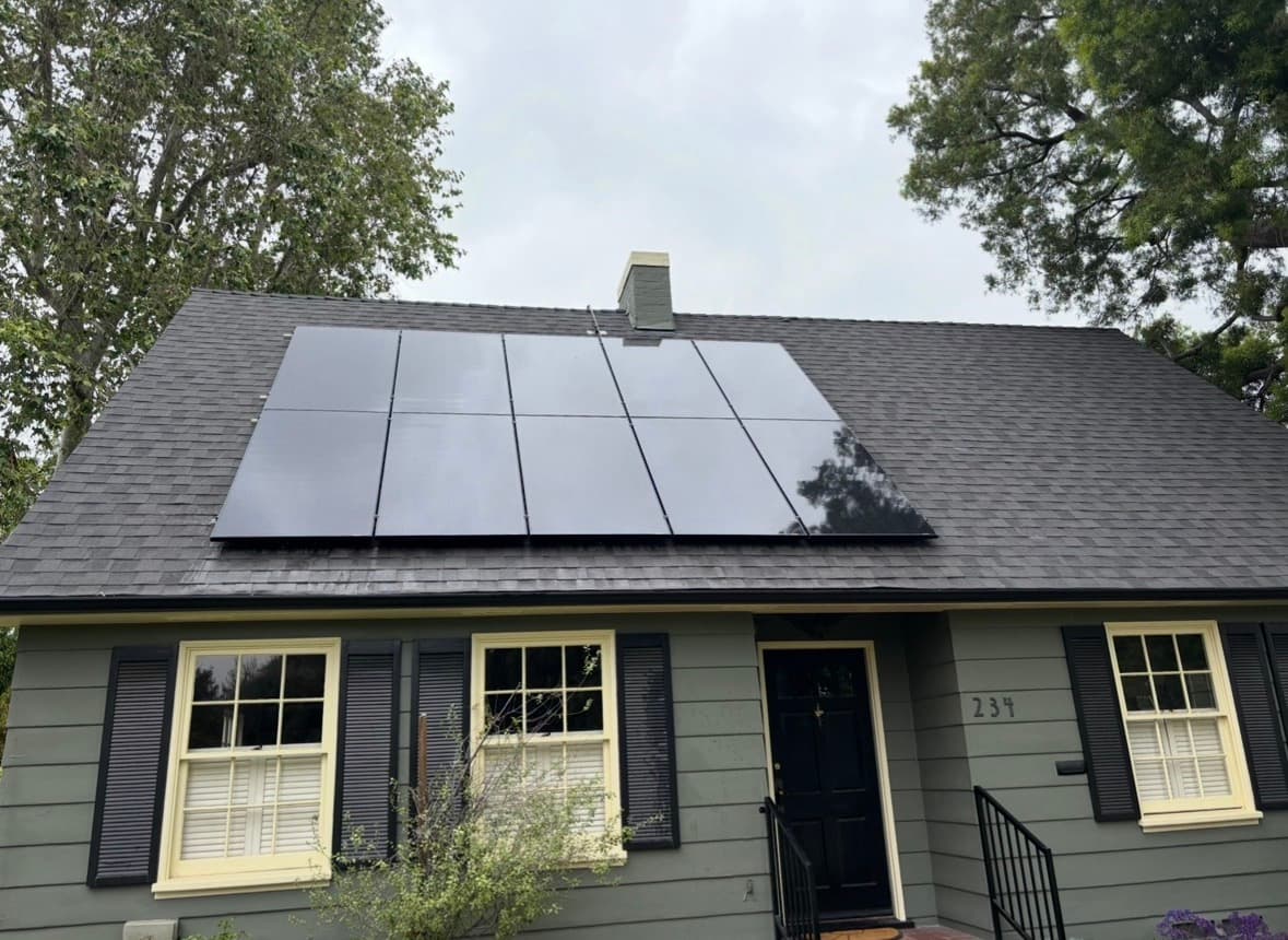 Large black solar panels on the dark roof of a house with olive green siding.